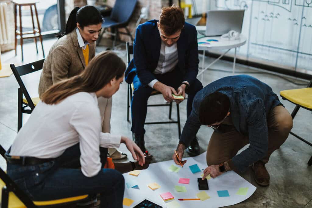 Vier Kollegen und Kolleginnen sitzen zusammen um einem großen Papierbogen und arbeiten ein Konzept aus.